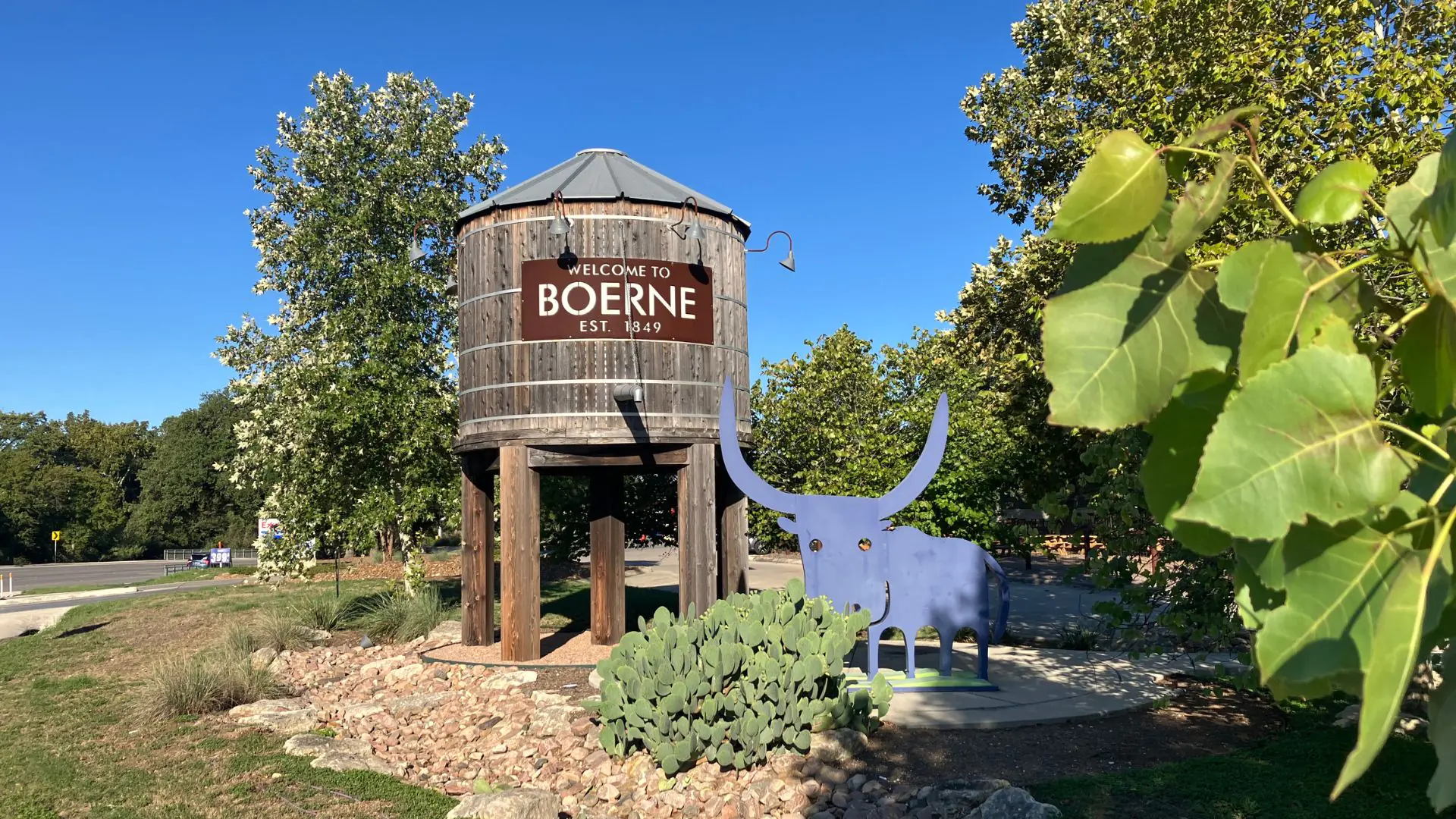 Welcome to Boerne sign on a wooden water tower beside a metal longhorn sculpture