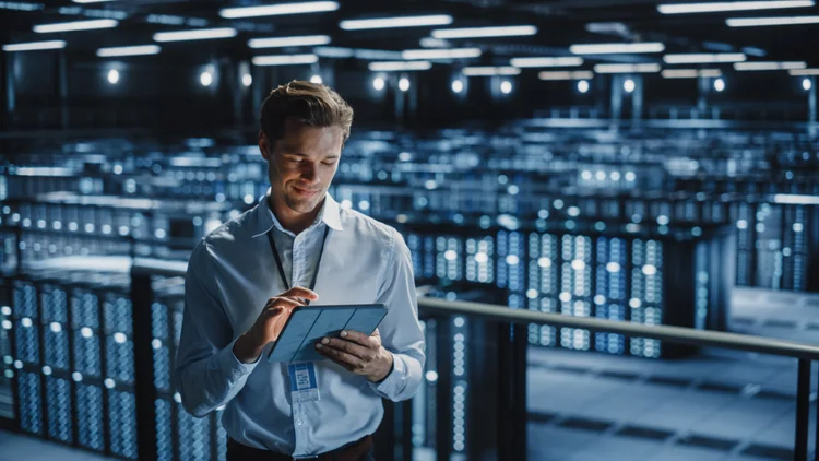 IT infrastructure specialist reviewing systems on a tablet in a data center